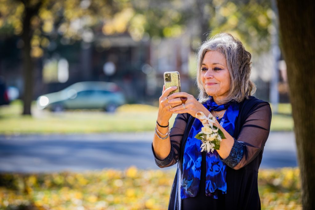 Mother of the bride smiles while taking a video on her phone