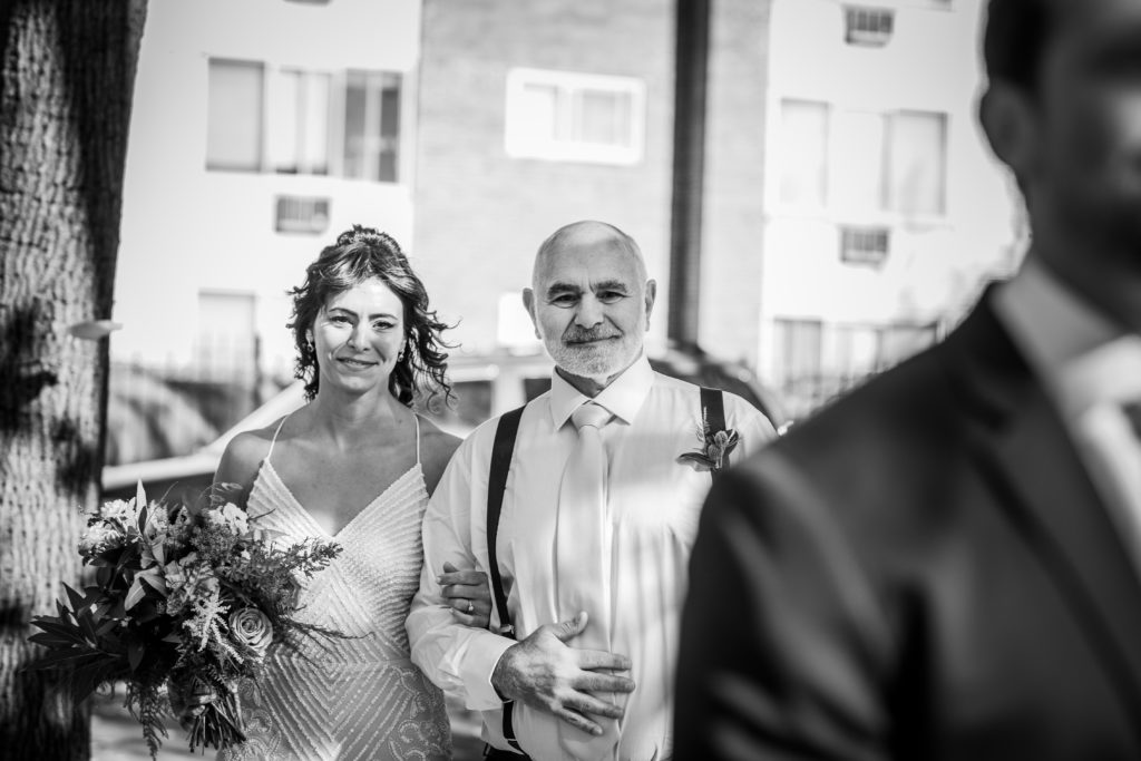 The bride and her father walk toward the groom with his back turned