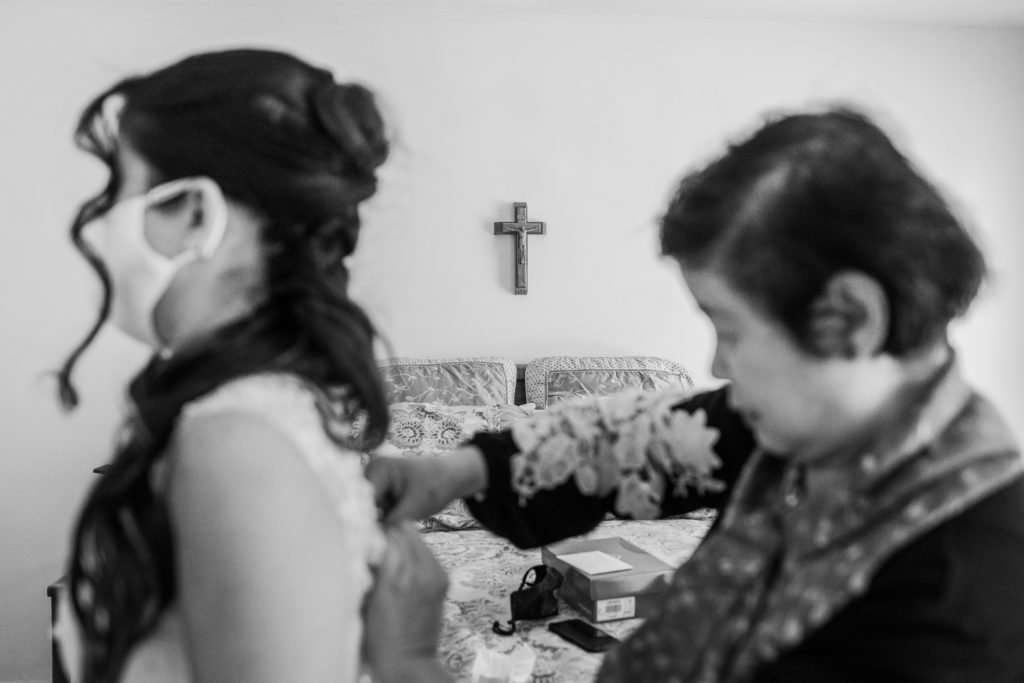 Mother buttoning up the bride's dress with a cross in the background
