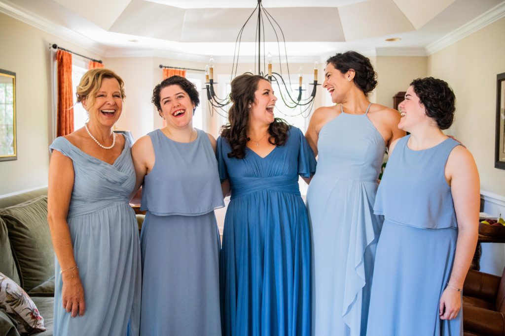 Bridesmaids in blue dresses laugh in a living room