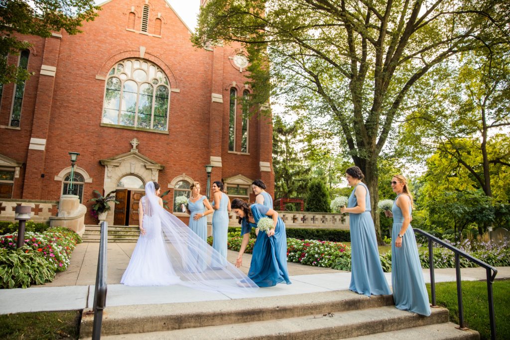Bridal party helping bride walk up the church steps 