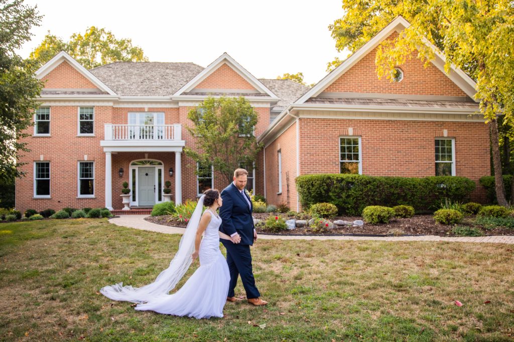 Bride and groom walking and holding hands in front of a house in Lake Bluff