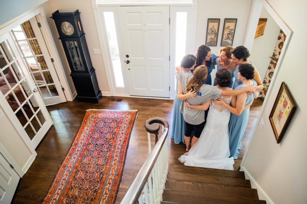 Bride and bridesmaids circle up for a prayer at the bottom of the stairs