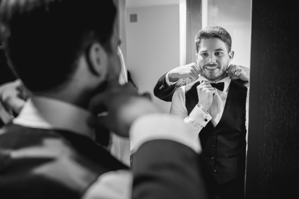 Groom putting on bowtie in the mirror
