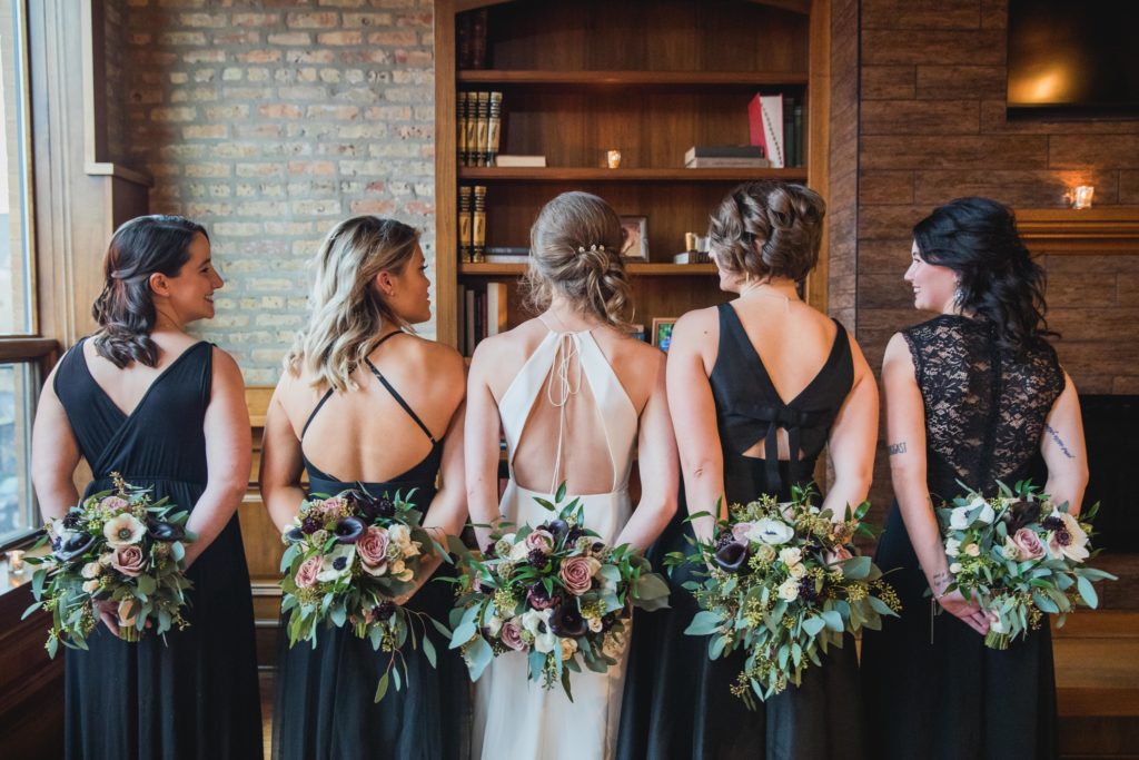 Bride and bridesmaids holding flowers behind their backs at Revolution Brewing