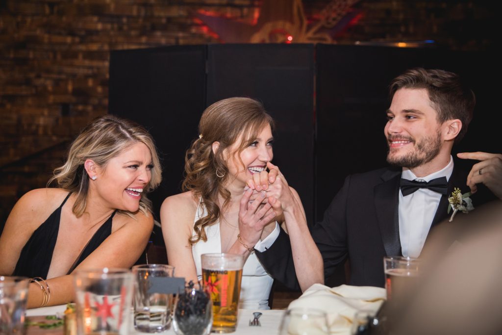 Bride and groom laughing at the dinner table with the Maid of Honor