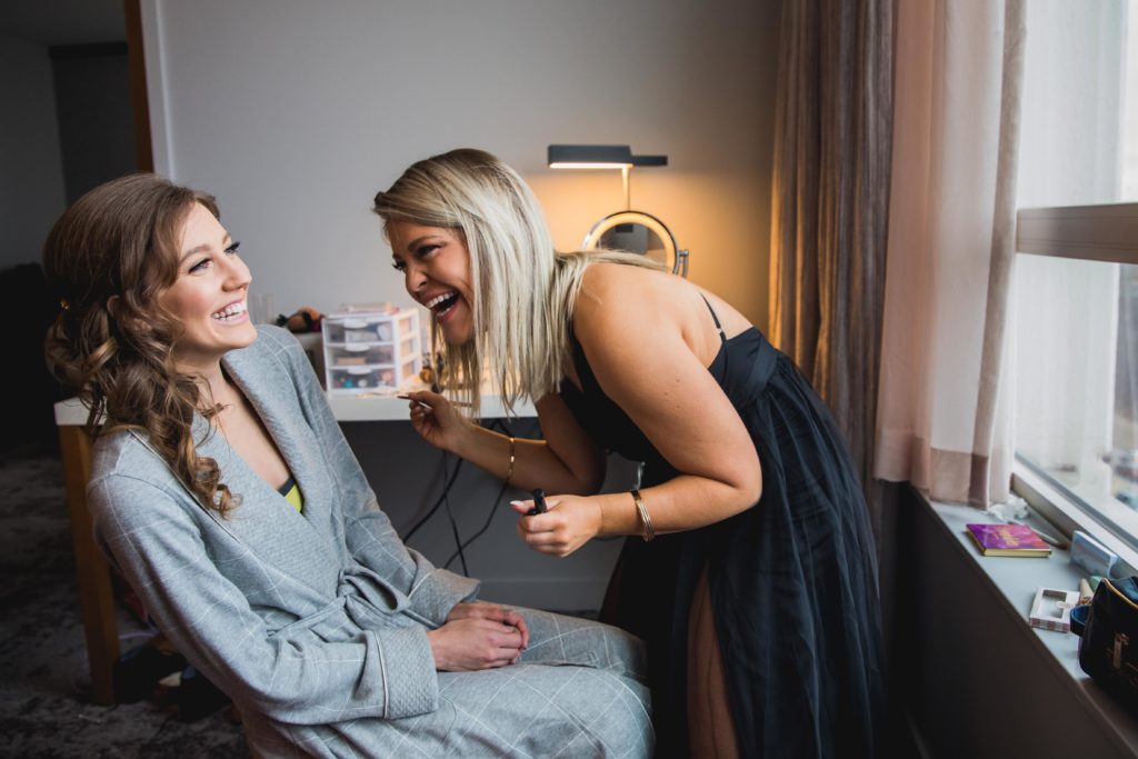 Bride laughing while her best friend does her makeup