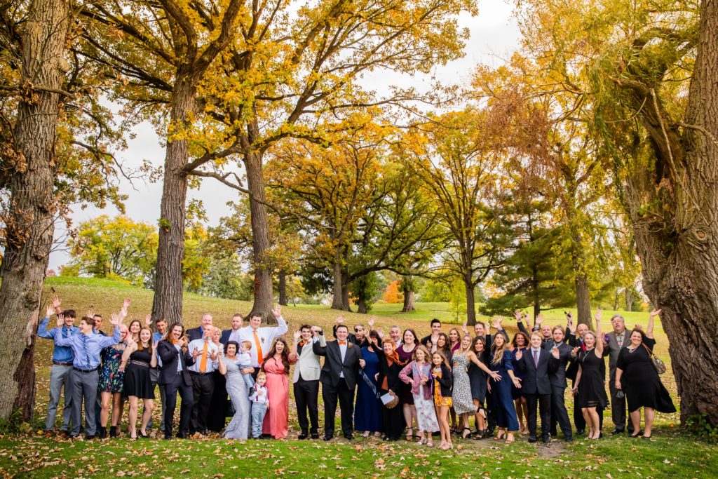 Entire wedding gathers for a group photo by some trees