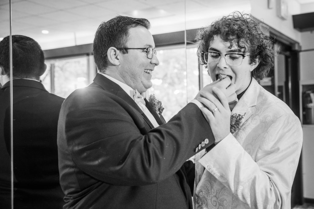 Groom laughs as he feeds his husband a piece of cake