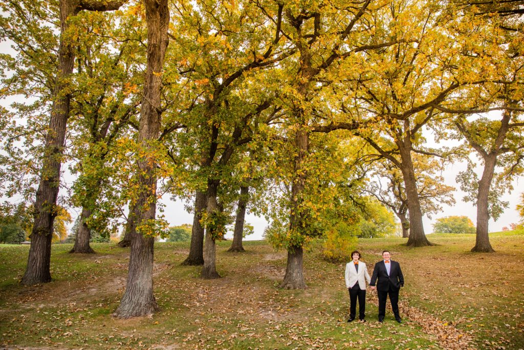 Grooms holding hands beneath fall foliage at their Silver Lake Country Club Wedding