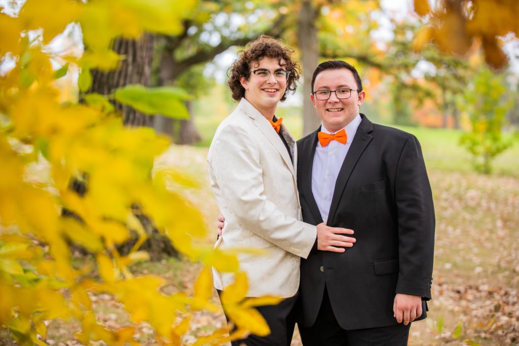 Grooms smiling for a portrait behind yellow leaves at the Silver Lake Country Club