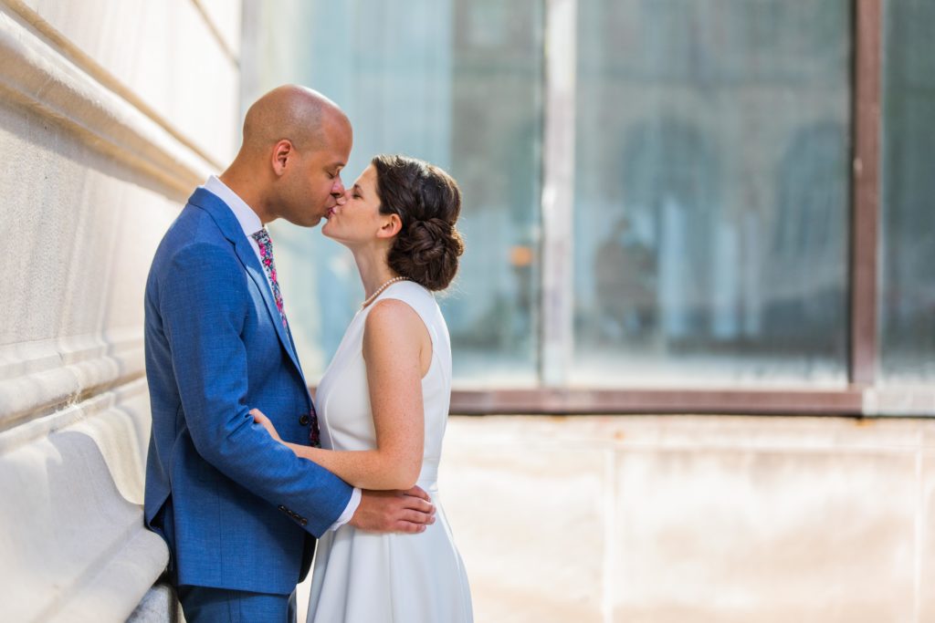Couple kisses while groom leans against a wall of the Art Institute