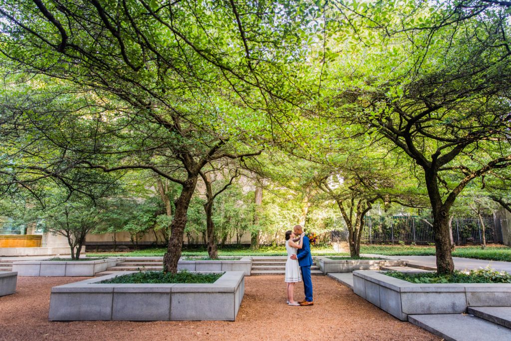 Bride and groom kiss on a bench underneath trees in the Art Institute South Garden