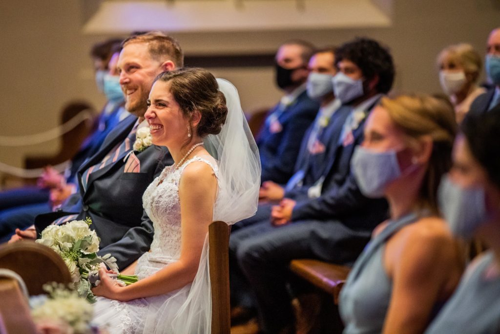 Bride laughing as she sits in a church while guests wear masks