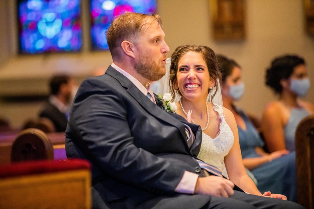 Bride laughing and smiling at the groom while they sit in church