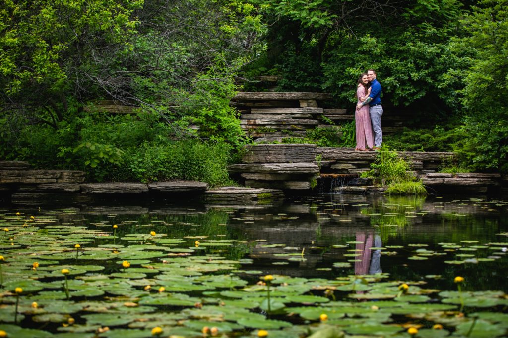 Couple holding each other while at the edge of a lily pond