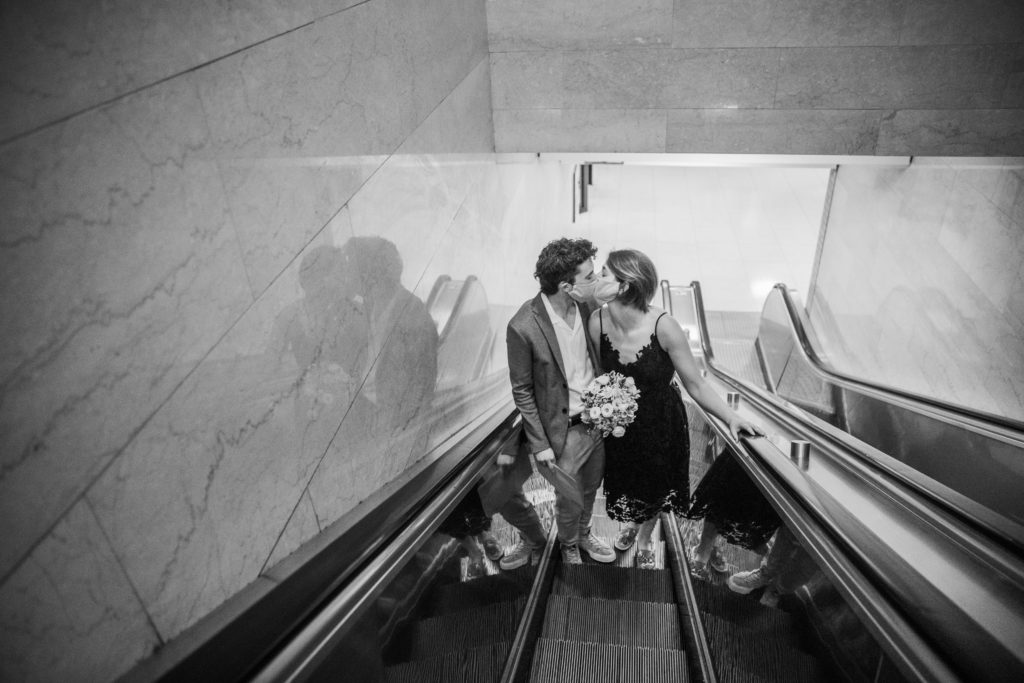 Couple kissing with masks on as they go up the escalator