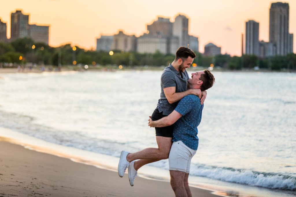 Man lifting up boyfriend and spinning him by the water while smiling at North Avenue Beach