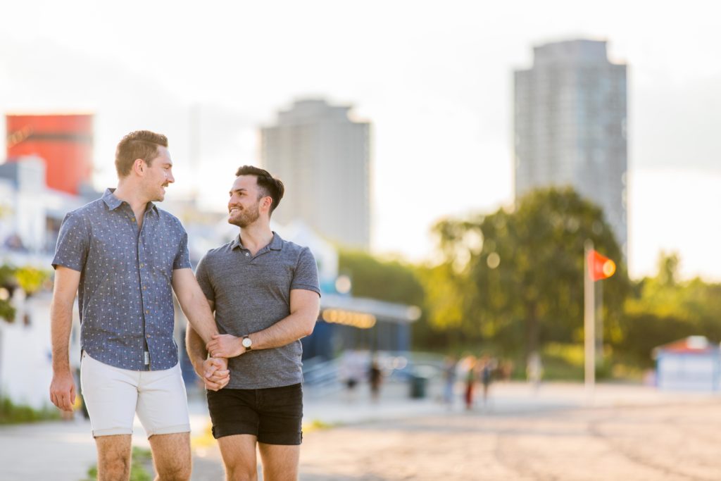 Men holding hands and smiling while walking together on the beach