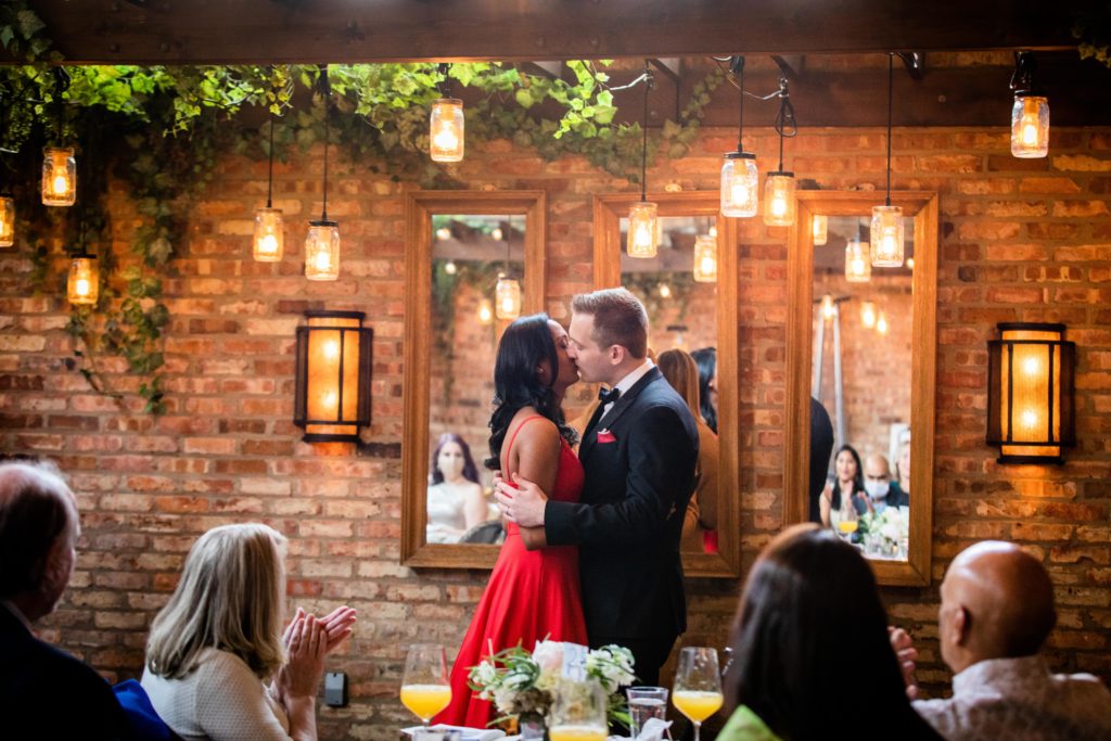 Bride and groom kiss while everyone claps in the back room at Stella Barra