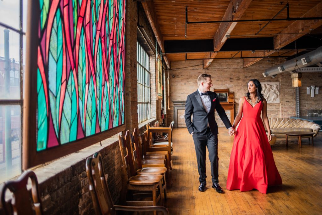 Bride and groom walk hand in hand by a stained glass window during their Salvage One Wedding Session