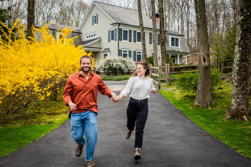 Couple smiling at each other while running down a driveway in Bedford
