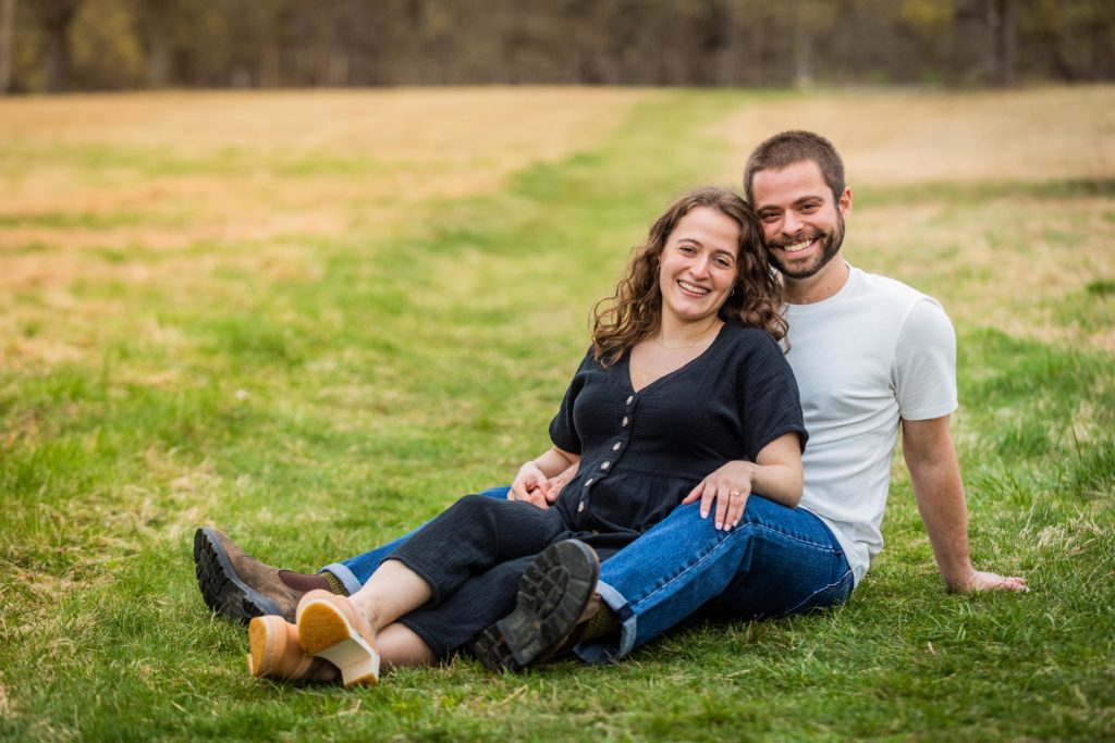 Couple smile as they snuggle together in a field