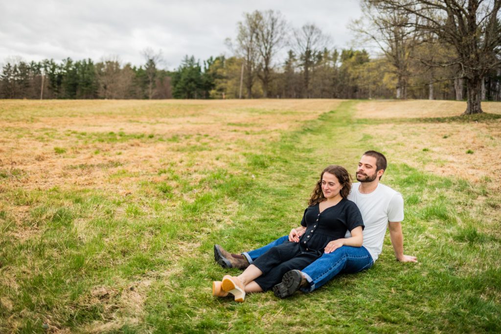 Woman sits in her fiancé's lap in Ward Pound Ridge Reservation during their engagement session