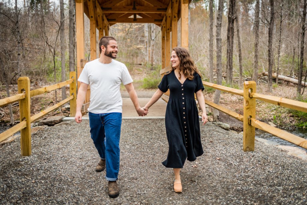 Couple look at each other and hold hands while walking over a wooden bridge