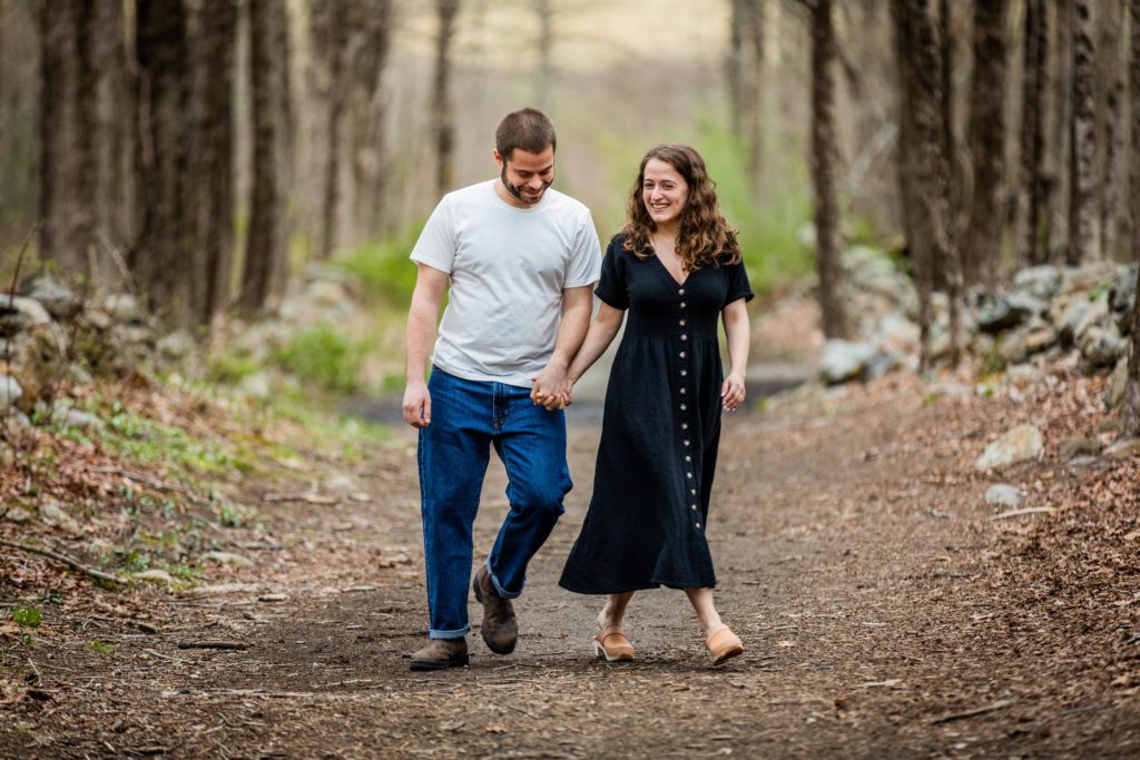Man and woman smile while walking through the woods