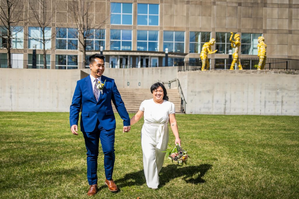 Bride and groom laugh while walking on a lawn in downtown Chicago