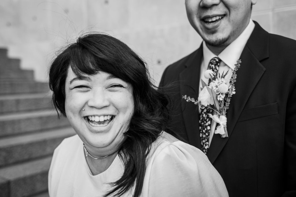 Bride laughs while husband laughs behind her