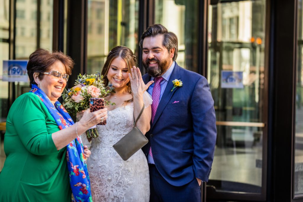 Family looking at a phone while bride shows off her ring