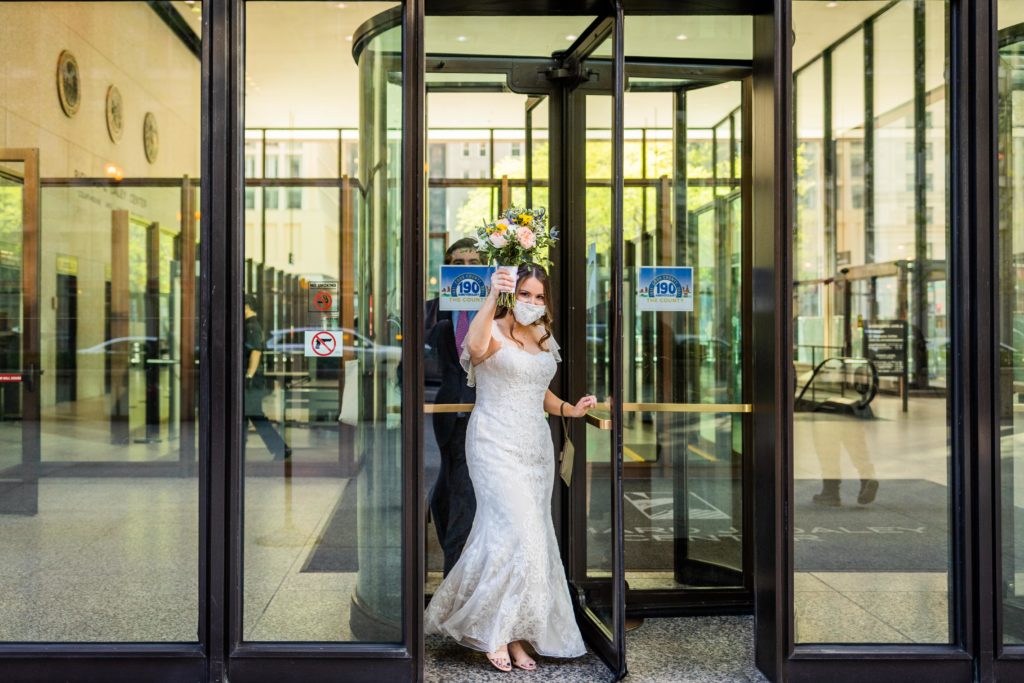 Bride walking out of city hall holding her bouquet up