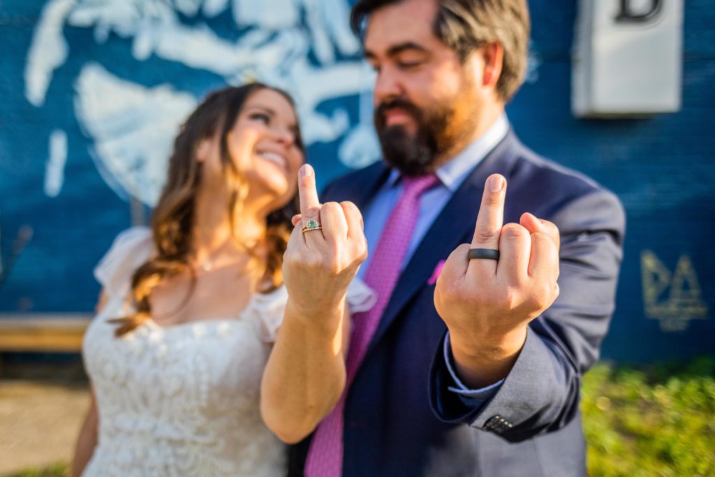 Couple holds up their ring fingers while smiling at each other