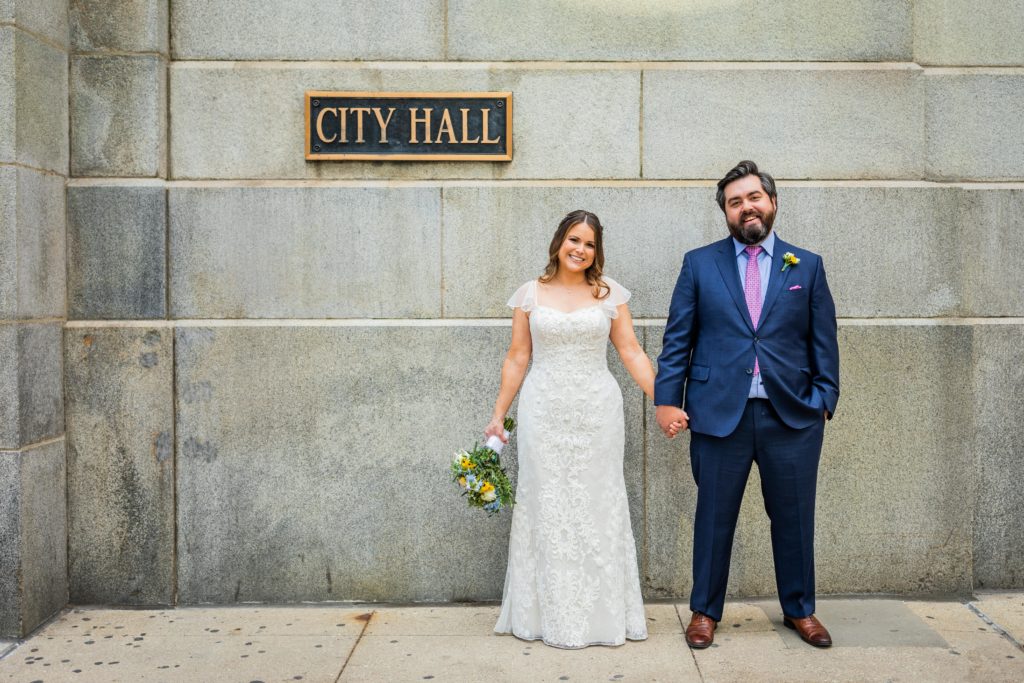 bride and groom smile while standing in front of the City hall sign in Chicago