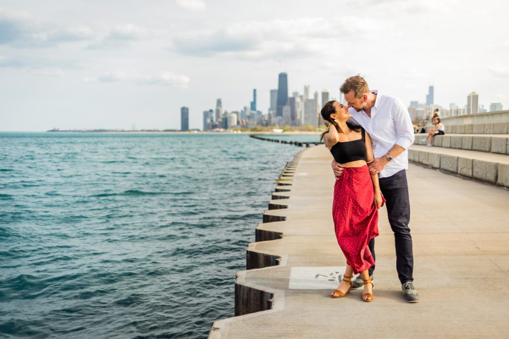 Man holds woman from behind as they smile at each other next to the lake during their Lincoln Park proposal
