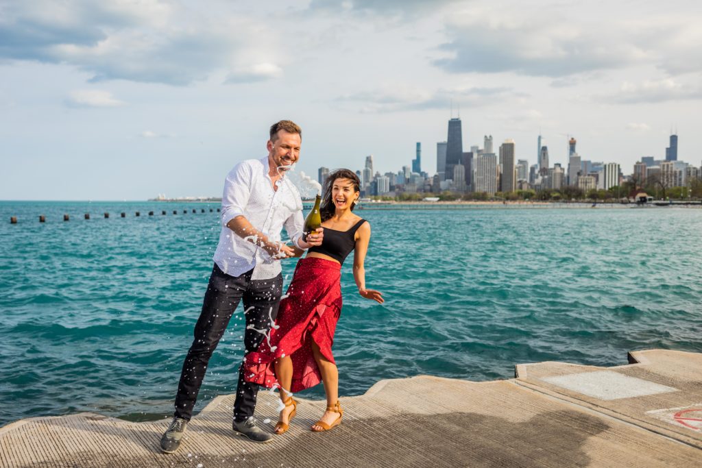 Man and woman pop champagne in front of Lake Michigan after their Lincoln Park Proposal
