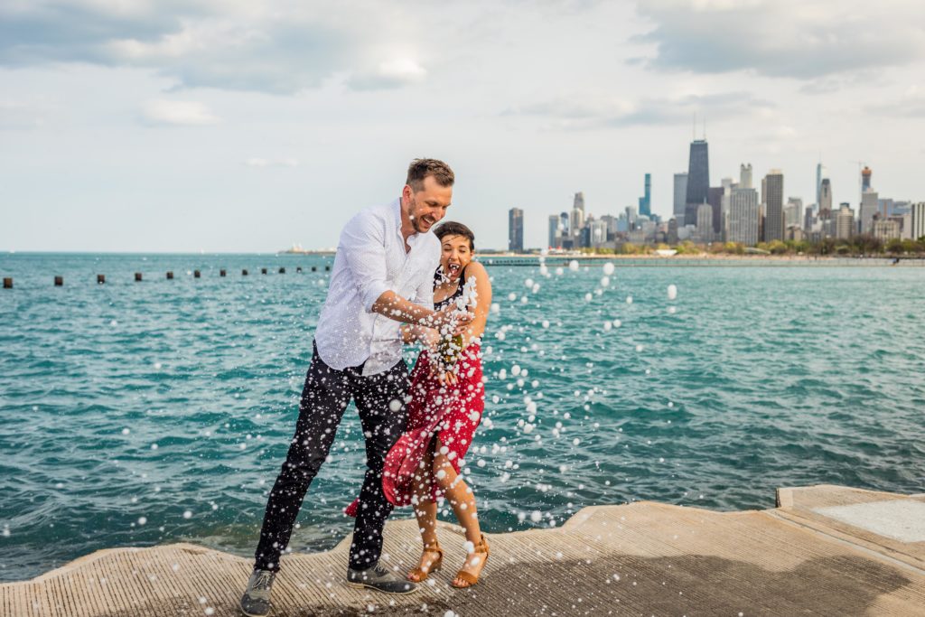Man and woman pop champagne and scream in front of Lake Michigan after their Lincoln Park Proposal