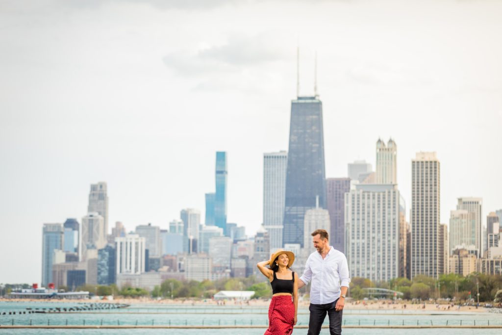 Couple laugh together as they walk next Lake Michigan with the Chicago skyline in the background