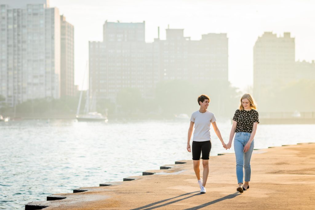 Gay women holding hands with the light behind them during their engagement session at belmont harbor