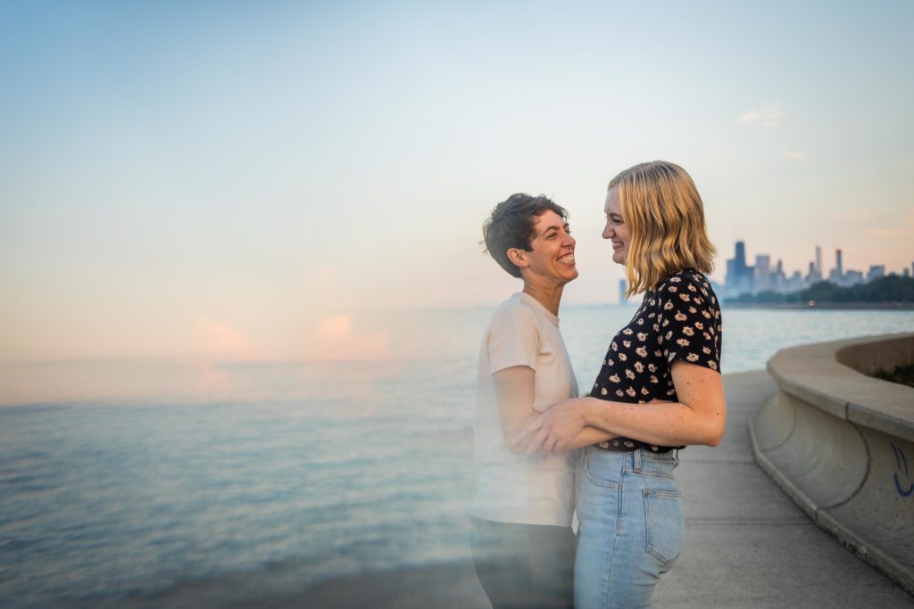 Queer women smiling and embracing during their engagement session at belmont harbor