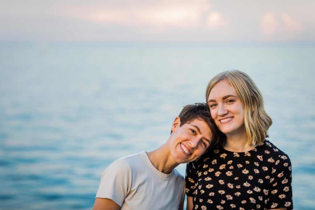 Queer women smiling with the lake behind them during their engagement session at belmont harbor