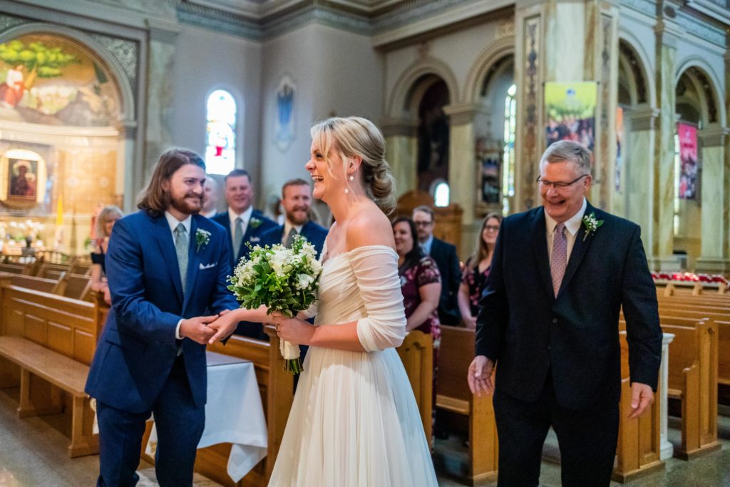 Bride laughs as her dad hands her off to the groom at St. Hyacinth Basilica