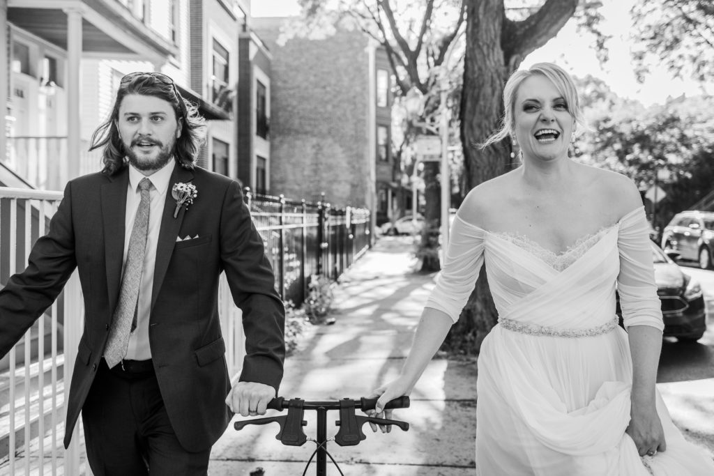 Bride and groom laugh while walking with scooter toward their Big Star reception