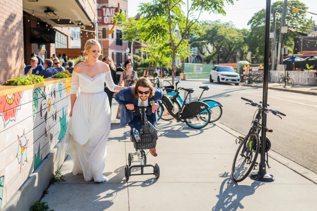 Bride walking next to the groom while he scoots down the sidewalk