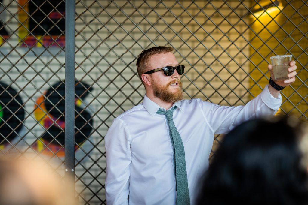 Best man lift a glass to raise a toast while wearing sunglasses