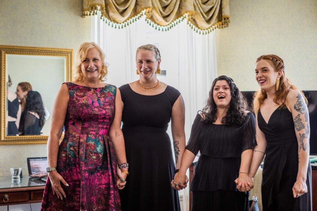 Bridesmaids hold hands and gasp as they see the bride for the first time