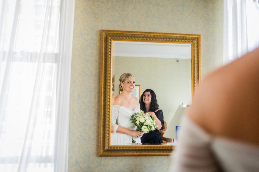Bride and bridesmaid smile in the mirror
