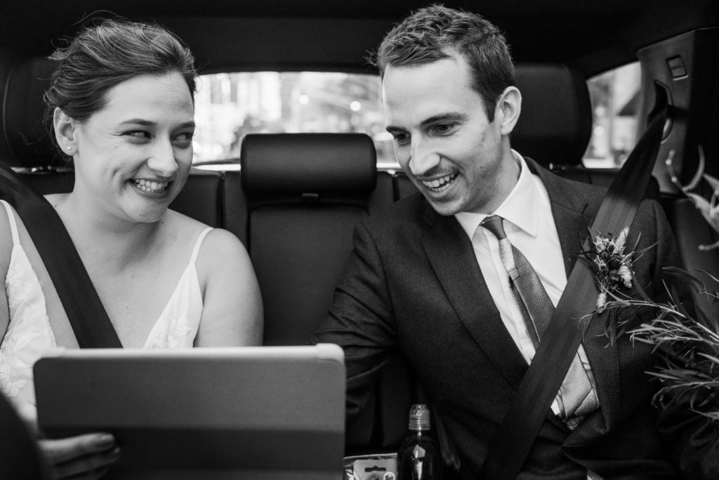 Bride and groom watching an ipad in the back of a car on the way to their Big Delicious Planet wedding